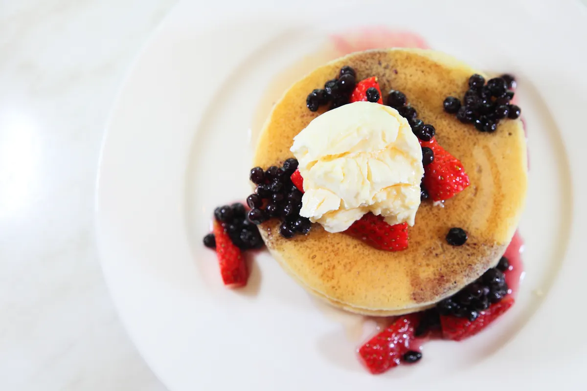 Stack of golden pancakes topped with berries and a scoop of ice cream on a white plate