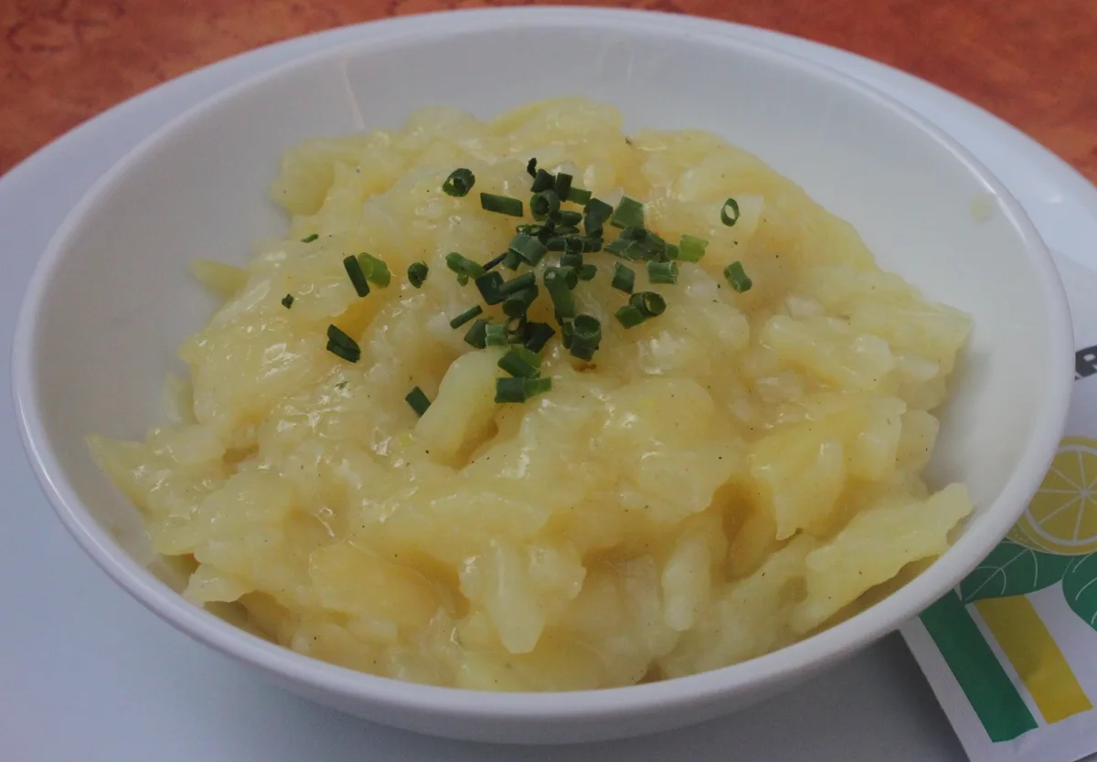 Creamy potato salad garnished with chopped chives in a white serving bowl
