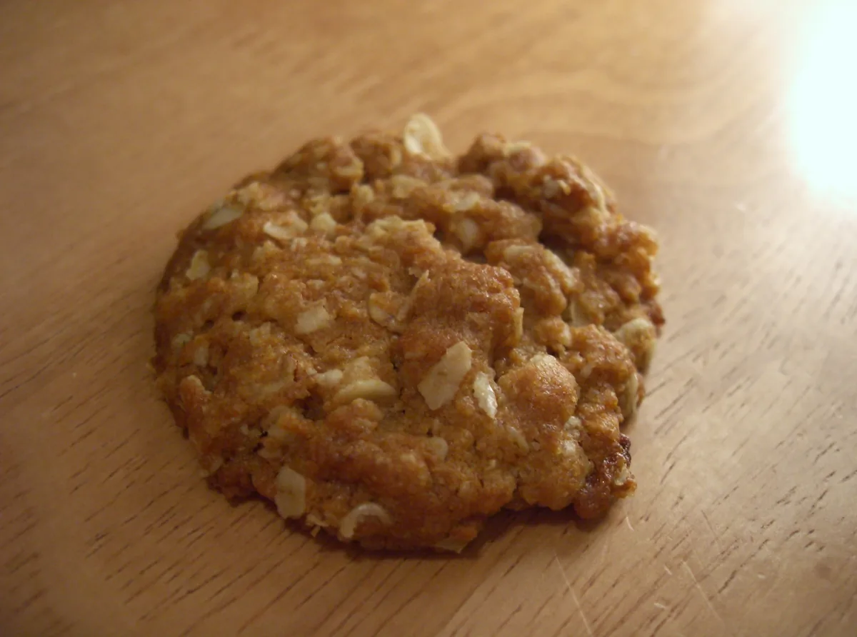 Single golden oat biscuit on a wooden table; the rights-cleared source photo shows a coconut-free variation
