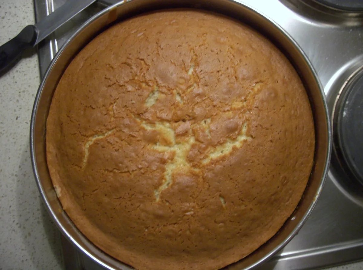 Round unfrosted vanilla butter cake with a deeply golden top in a metal cake tin